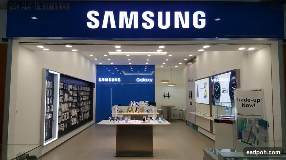 Storefront with illuminated 'SAMSUNG' sign above entrance; interior visible showing product displays, Galaxy branding wall, trade-up promotion signage, and retail shelving.
