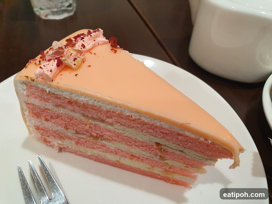 Slice of layered pink cake with peach glaze and rose petals