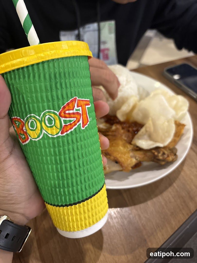 Hand holding Boost drink with food in background