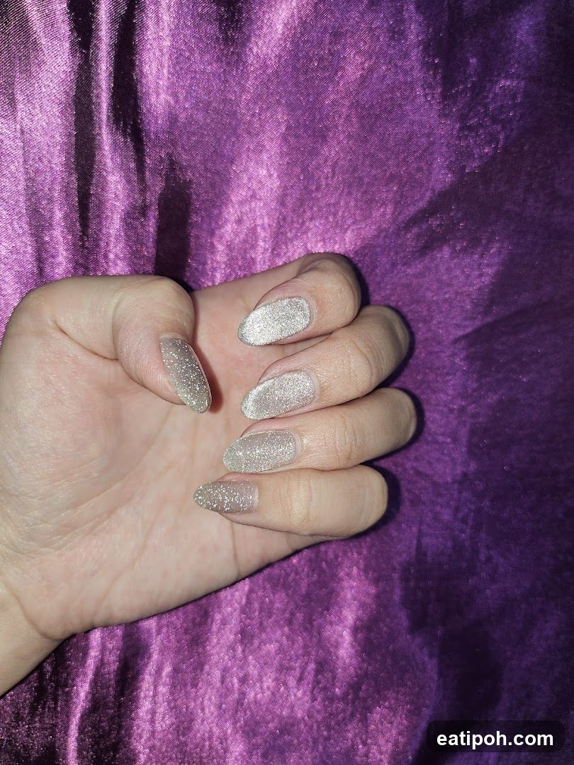 Hand with glitter nails on purple fabric