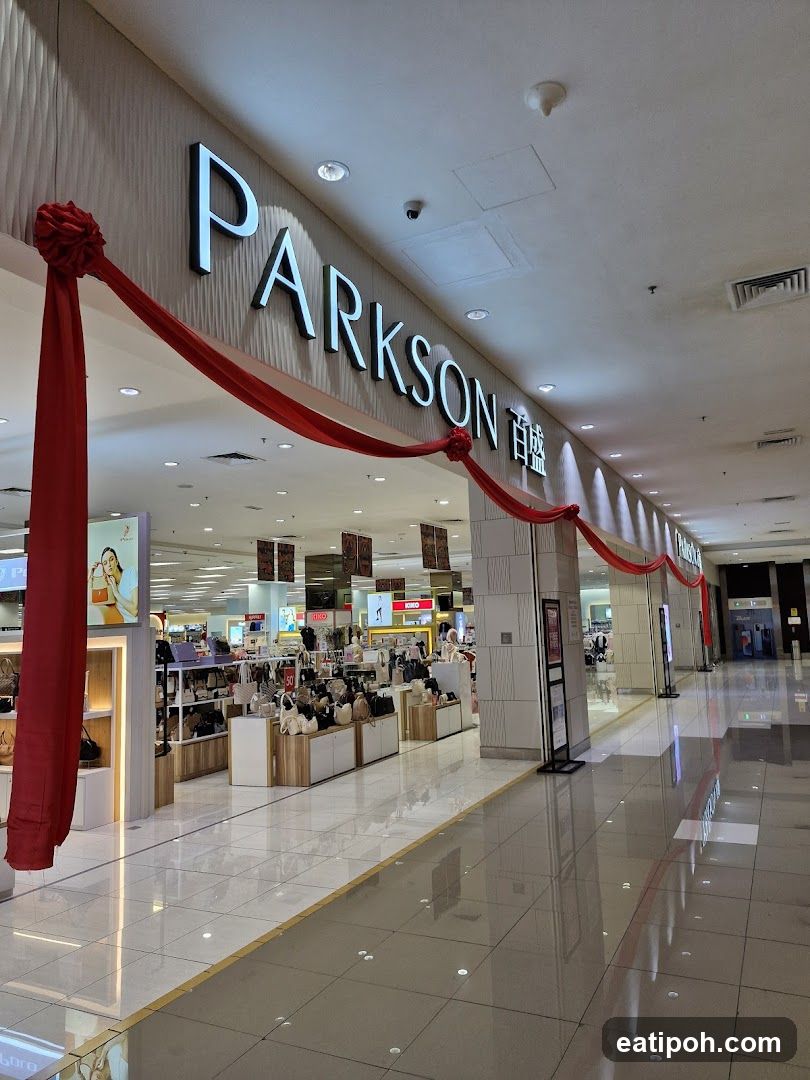 The exterior of a Parkson department store, with large illuminated signage spelling out "PARKSON" above the entrance. Red ribbons are draped across the facade, suggesting a festive occasion. Inside, displays of handbags and other merchandise are visible, along with promotional signage. The store appears to be located within a shopping mall, indicated by the polished floors and ceiling architecture.