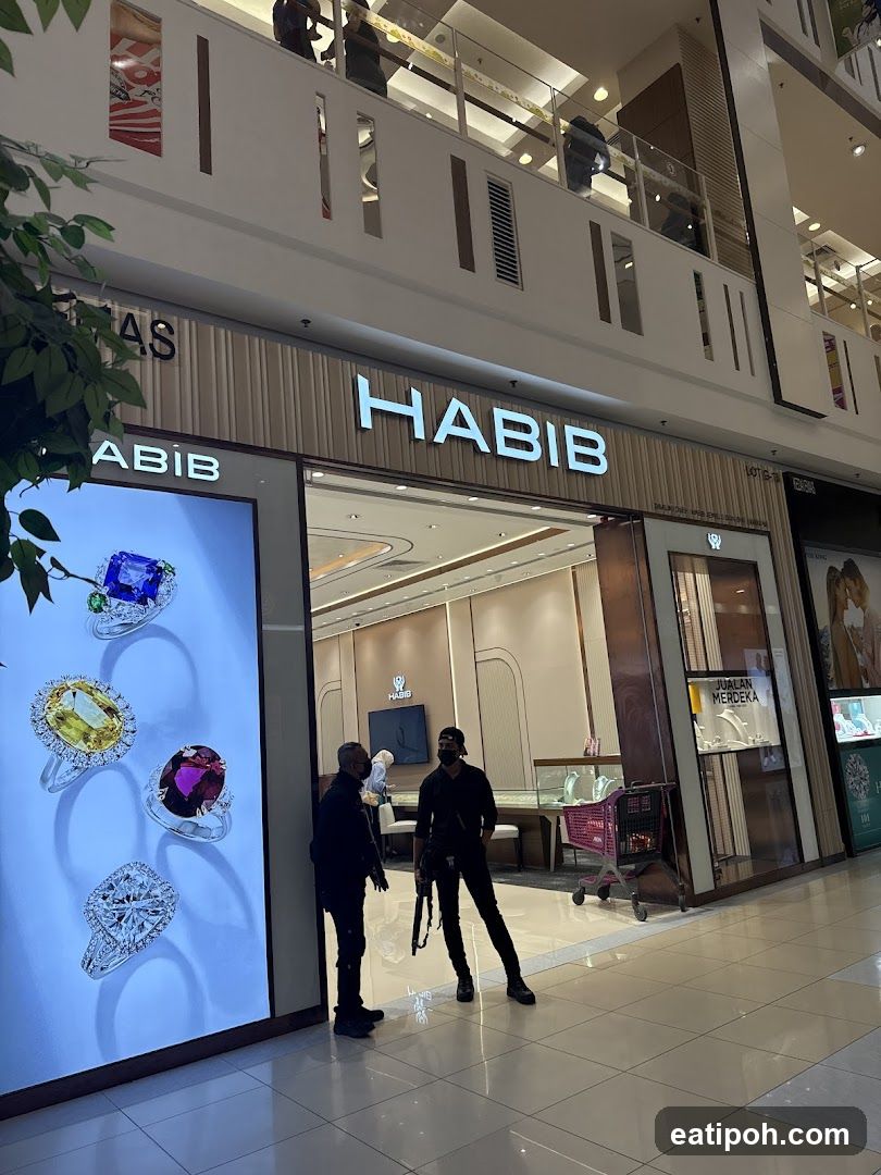 The exterior of a Habib jewelry store in a mall. The store has a large illuminated display of rings on the left and the store name "HABIB" prominently displayed above the entrance. Two individuals are standing near the entrance.