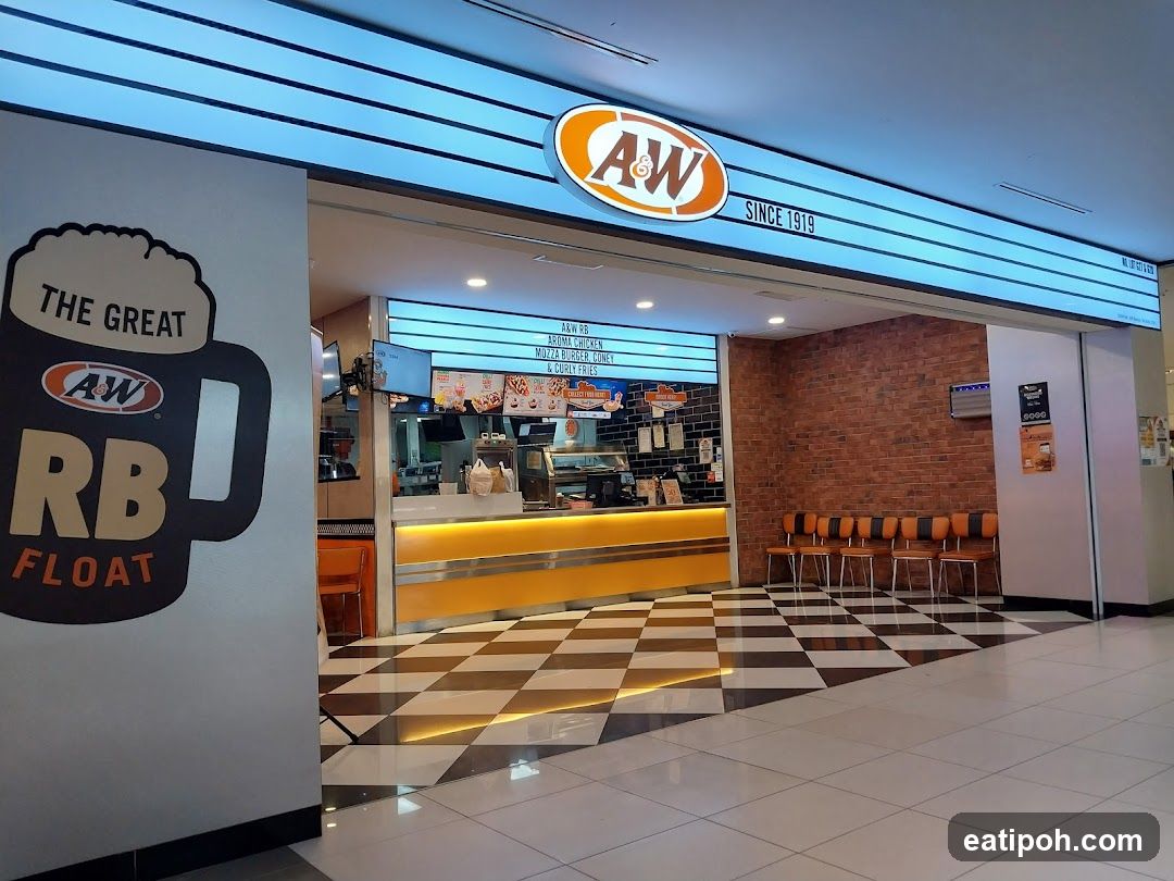 The exterior of an A&W restaurant with its prominent signage. A large graphic of a root beer float is on the left wall, and the main A&W logo with "SINCE 1919" is above the entrance. The counter area is visible with menu boards and seating.