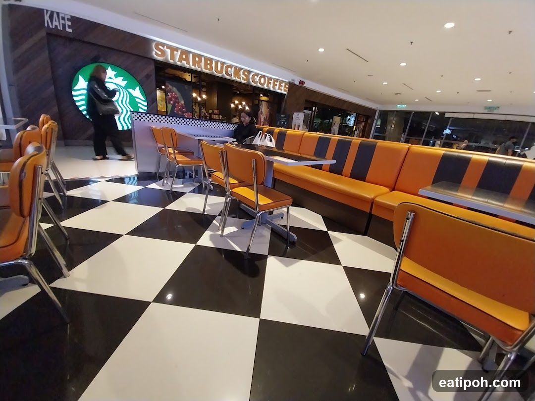 The exterior of a Starbucks Coffee shop with a prominent Starbucks logo and signage. The interior seating area features orange and black booths and chairs, with a black and white checkered floor. A person is walking into the shop.
