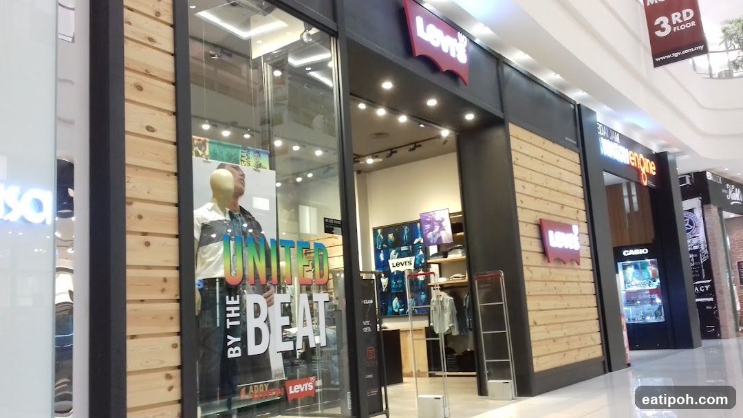 The exterior of a Levi's store in a mall. The store has a wooden facade with the Levi's logo prominently displayed. A mannequin in the window is wearing a jacket and jeans, with the text "UNITED BY THE BEAT" visible. Other store fronts are visible to the right, including Casio and what appears to be a cinema advertising the 3rd floor.
