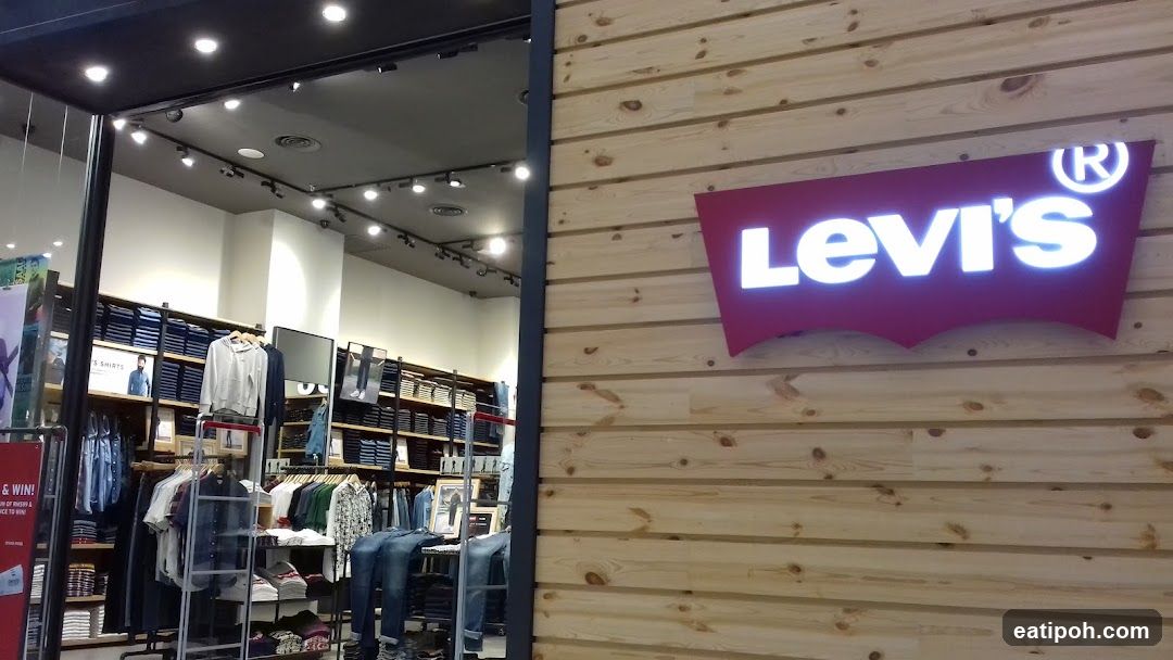 A large, illuminated Levi's logo is displayed on a wooden plank wall, serving as the exterior signage for the store. Through the open entrance, racks of folded jeans and hanging shirts are visible, along with displays of denim products.