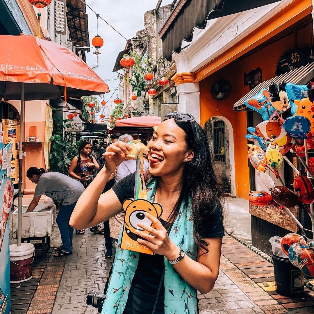 The narrow lane filled with colorful umbrellas, string lights, and heritage shophouses